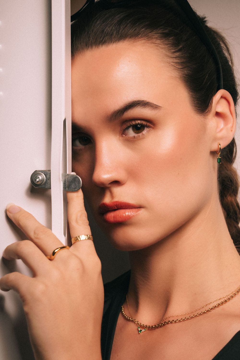 Modern portrait with gold jewelry and red lipstick against minimalist door setting.
