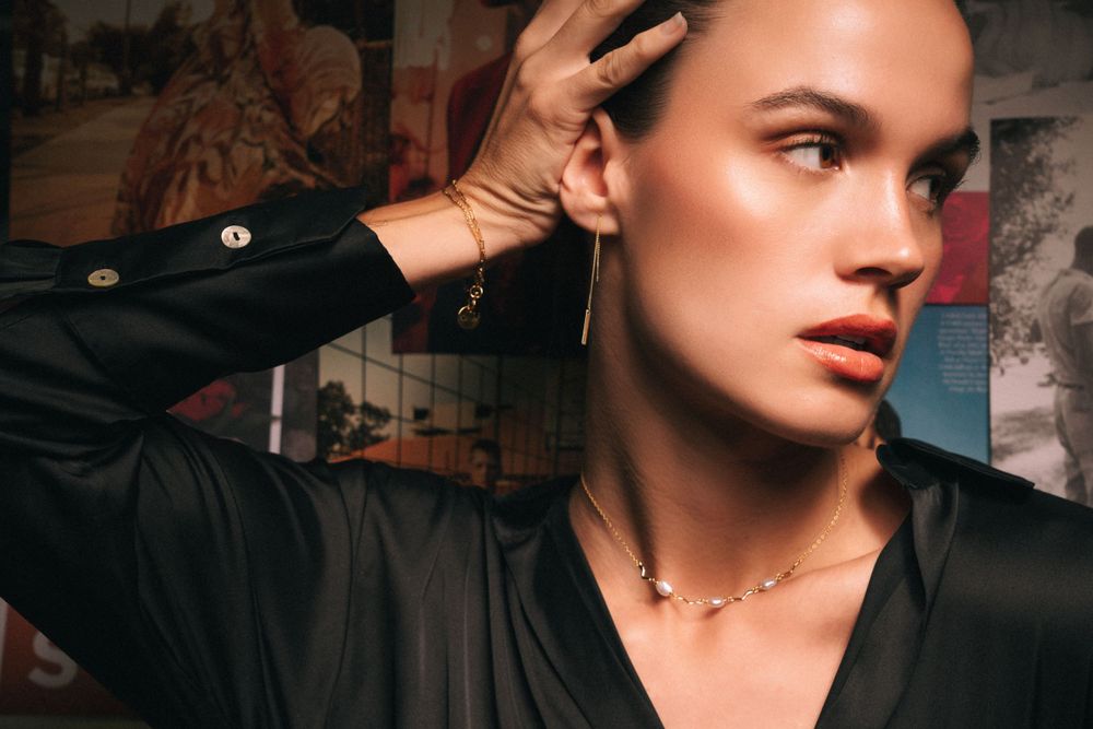 Dramatic fashion photo with dainty jewelry and black shirt against textured background.
