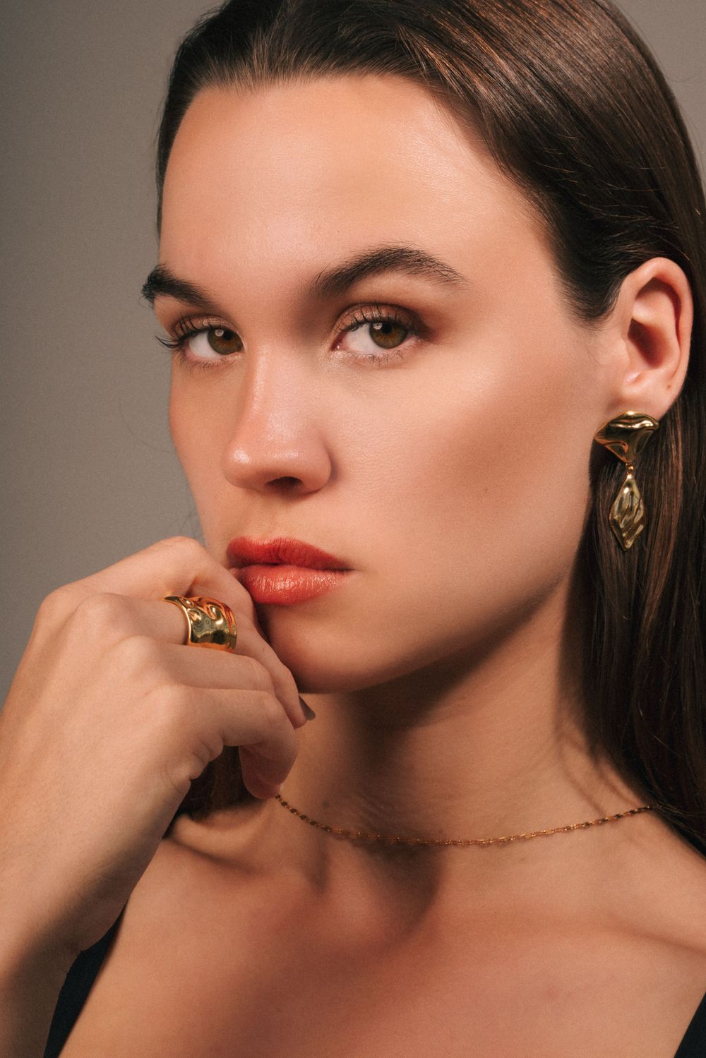 Beauty portrait highlighting statement jewelry and coral lipstick against neutral backdrop.