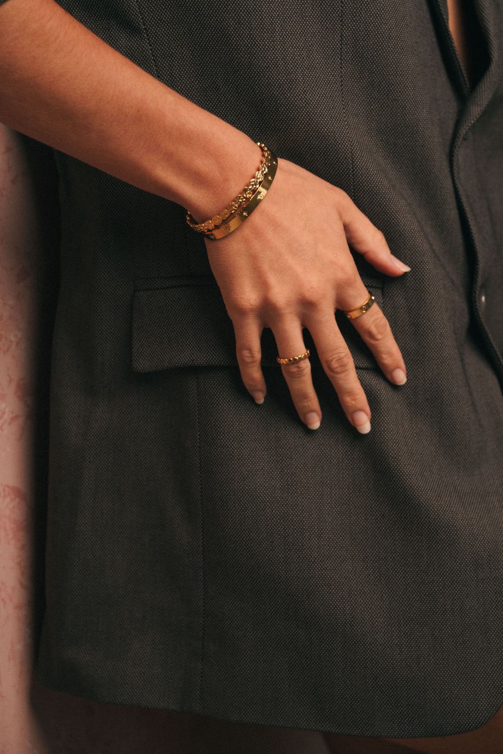 Close-up of hand wearing gold bracelet and rings with black blazer sleeve.
