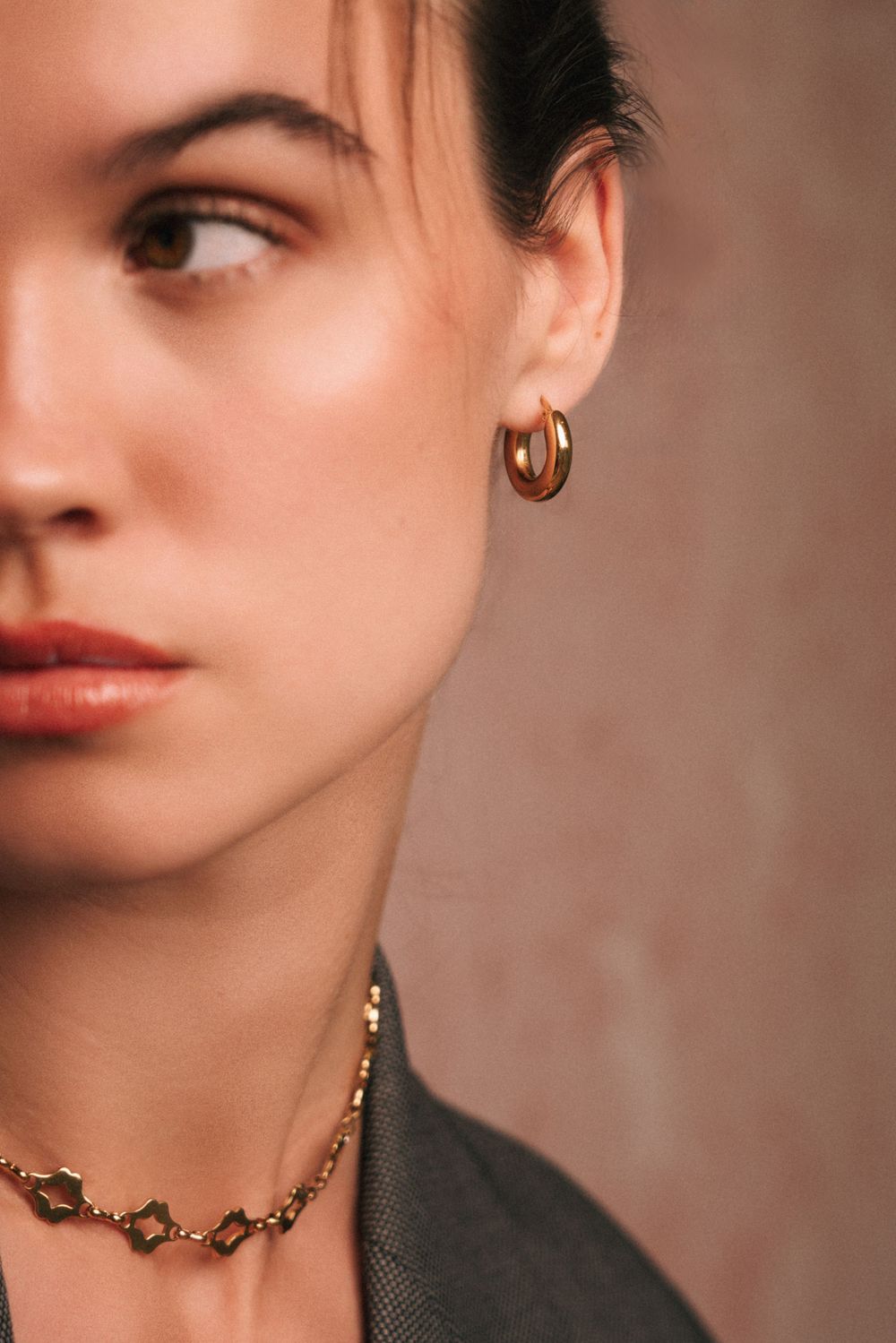 Side profile beauty shot featuring gold hoop earring and chain necklace.