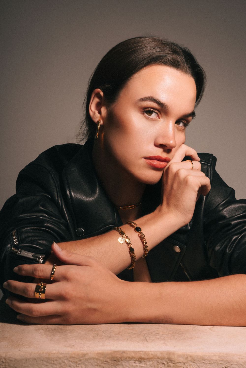 Fashion portrait with model in leather jacket against neutral background.