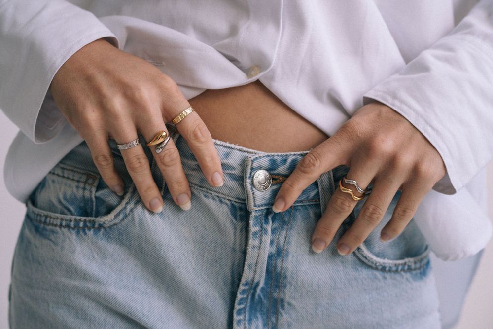 Hands wearing multiple rings shown against light denim and white fabric.