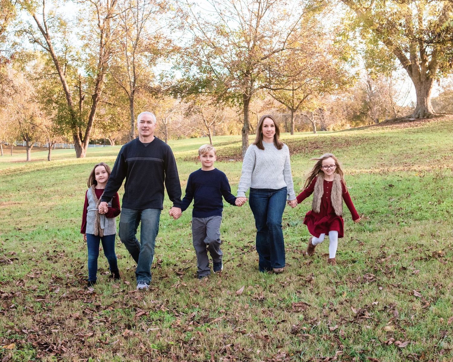 Family walking together holding hands through a fall landscape with autumn leaves on the ground.