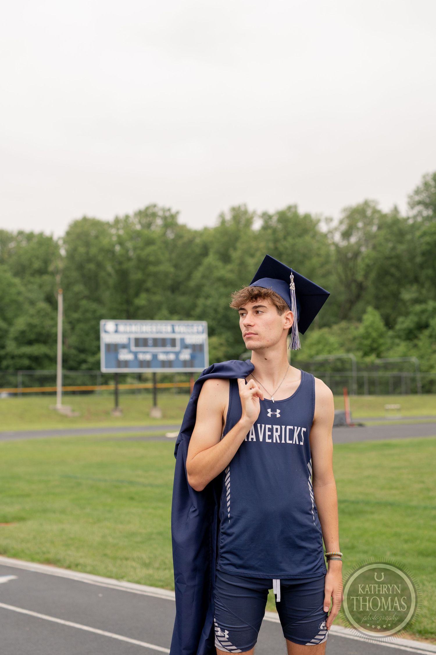 Student athlete in Mavericks jersey carries graduation gown over shoulder on track.
