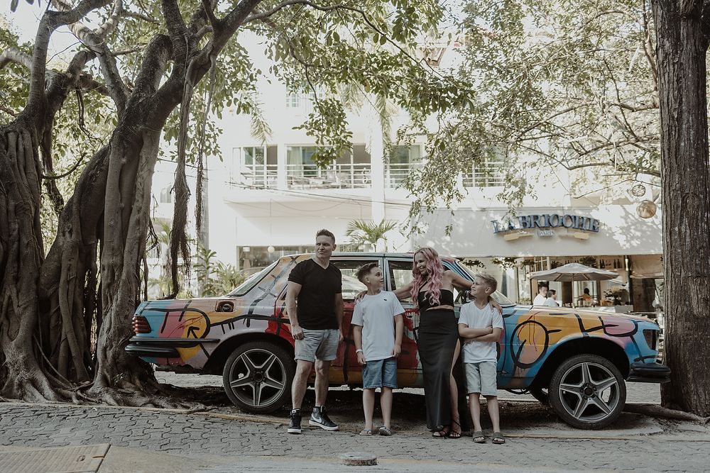 Family posing by vintage car at Residencia Art Project during Playa del Carmen editorial photoshoot.
