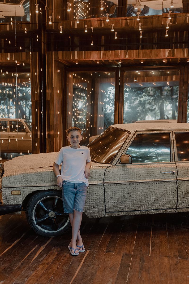 Boy posing by vintage car with string lights at Playa del Carmen family photography session.