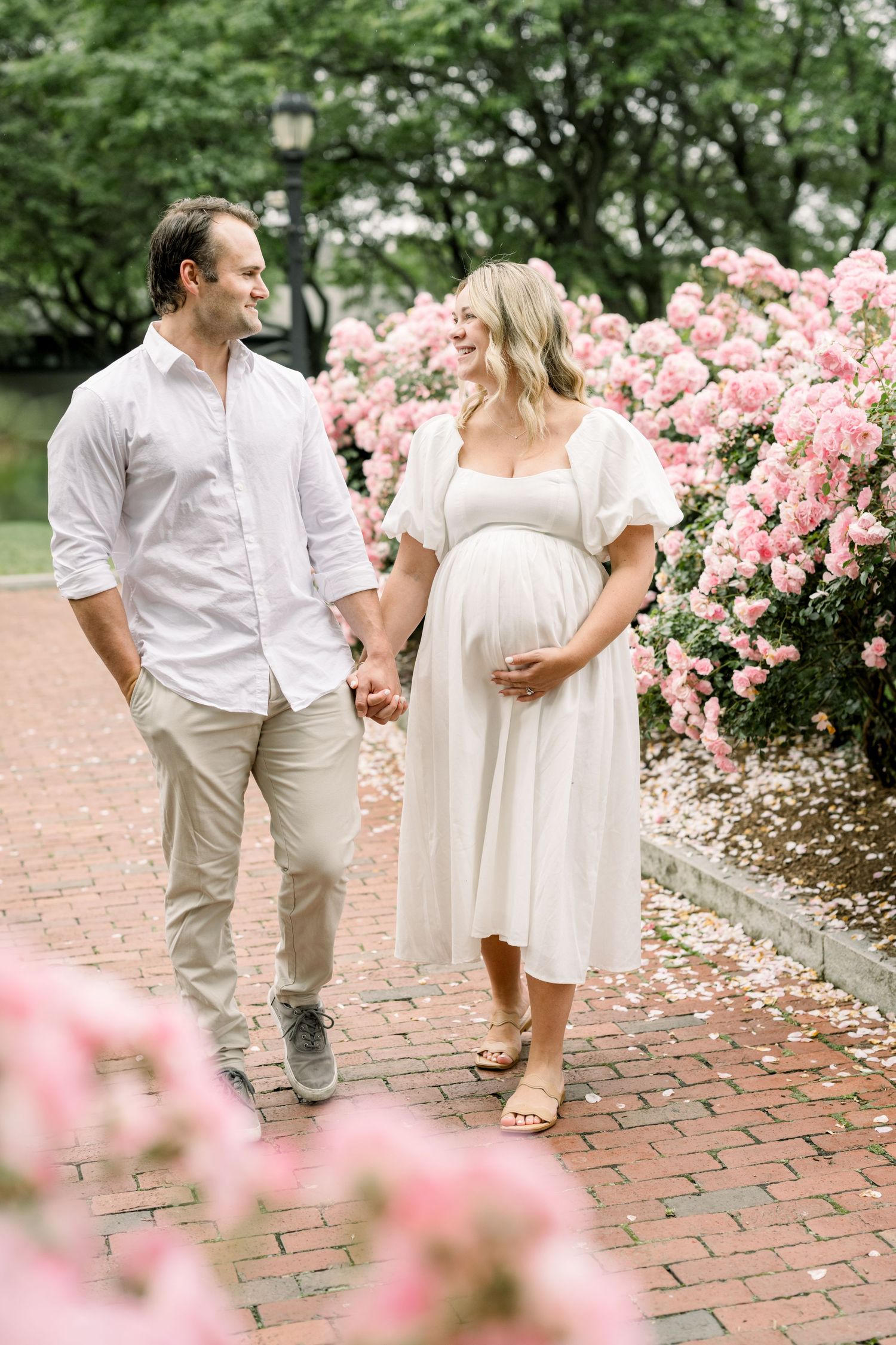 An elegant maternity portrait of a woman in a white dress and cream cardigan by the seaside.