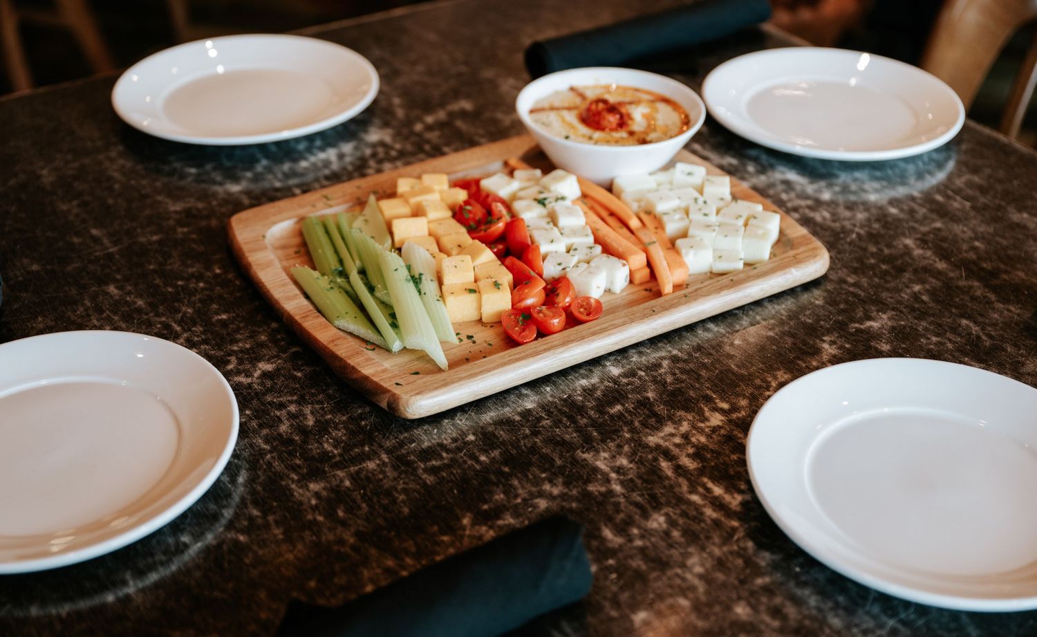A charcuterie board with cheese, meat, vegetables and crackers arranged on a dark wooden table.