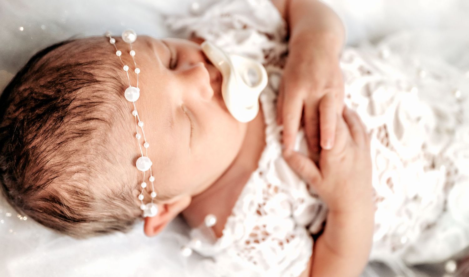 A sleeping infant with closed eyes lies peacefully in soft white lace bedding.