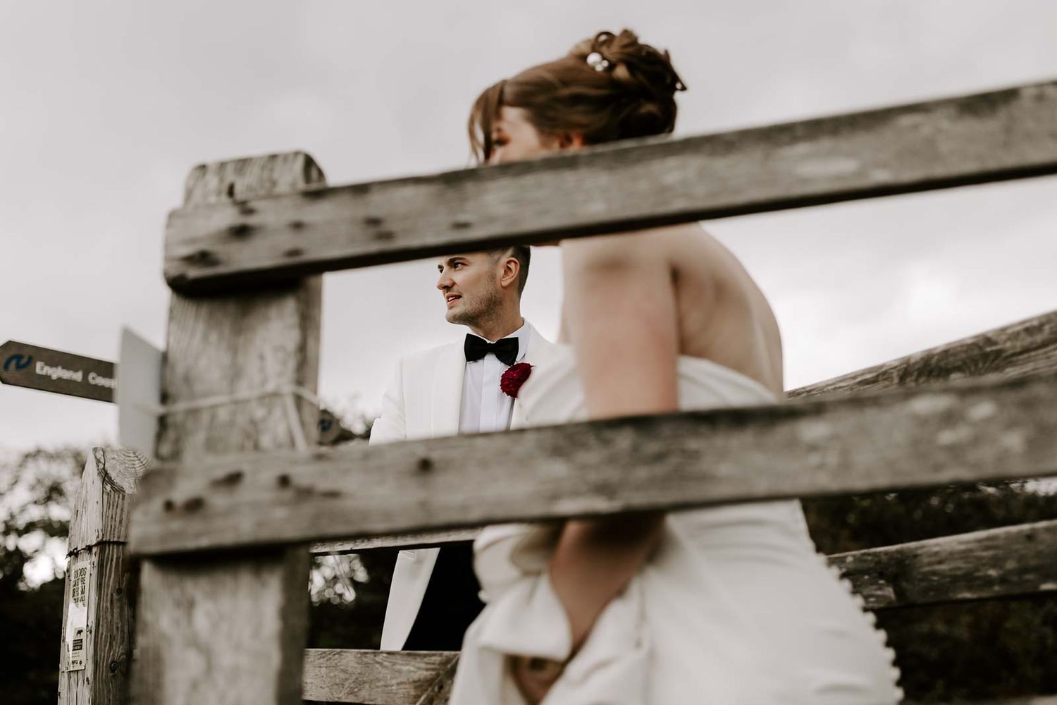 A couple in wedding attire stands between rustic wooden fences on their special day.