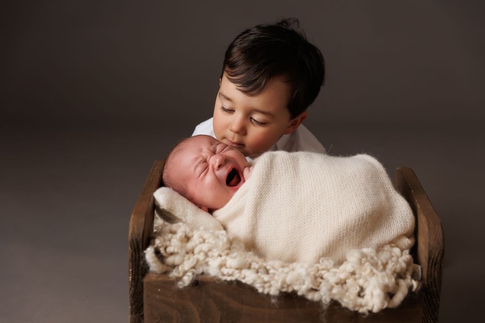 toddler brother looking at his newborn brother in a little crate on a dark grey background