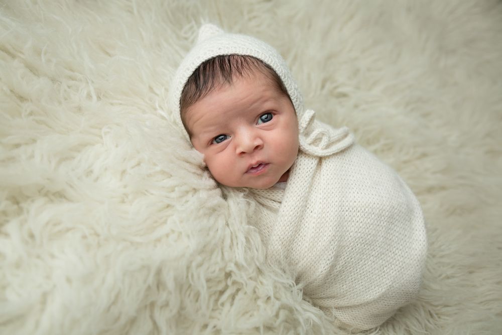 Newborn baby peacefully swaddled in a soft white blanket, resting on a cozy white fur surface.