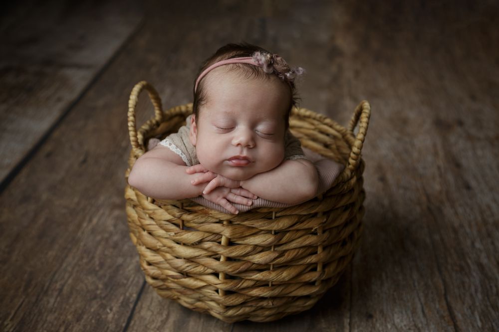 A peaceful newborn girl peacefully sleeps in a cozy wicker basket, wrapped in soft blankets.