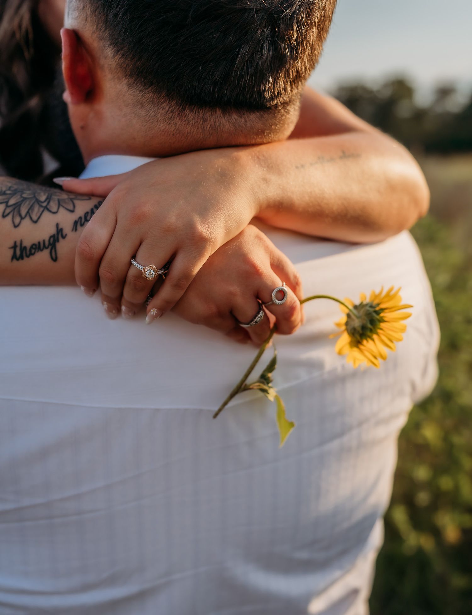 Close up of couple embracing with sunflower and visible tattoo.