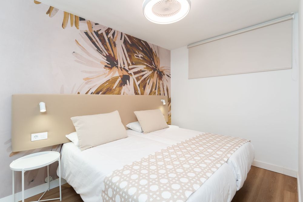 A bright and modern bedroom interior with white bedding, wooden accents, and natural lighting through large windows.