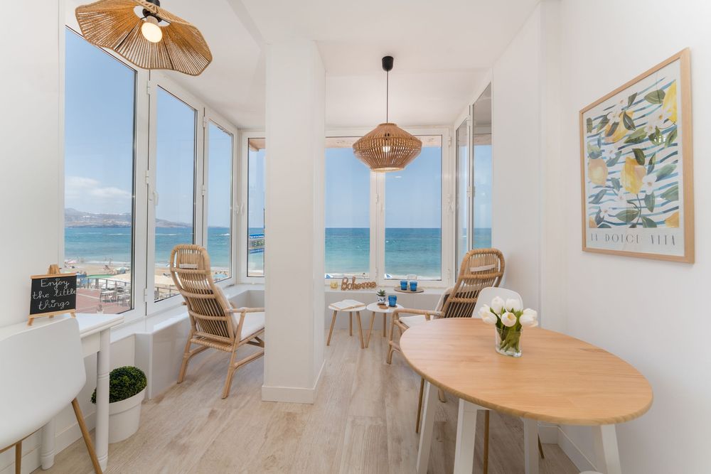 Bright coastal dining room with ocean views, rattan chairs, wooden table, and pendant lamp in a modern beachfront apartment.