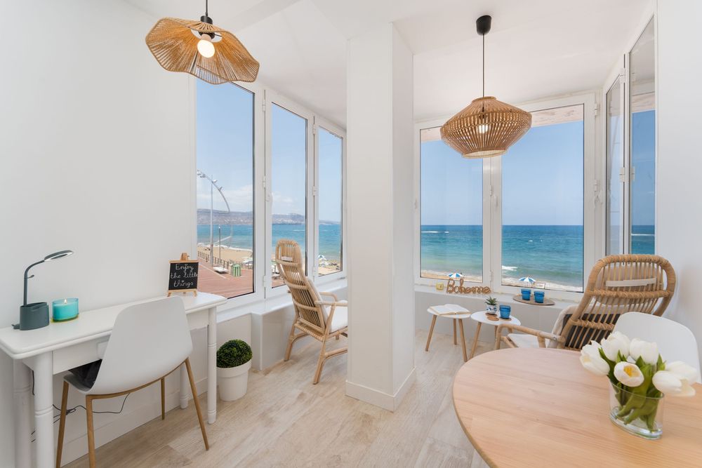 Bright coastal apartment with ocean views, wicker pendant lights, wooden furniture, and white walls.