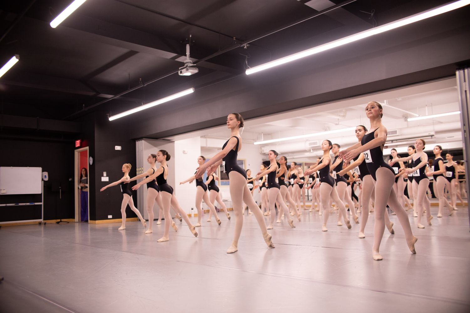 Large group of ballet dancers practice in formation during studio class.