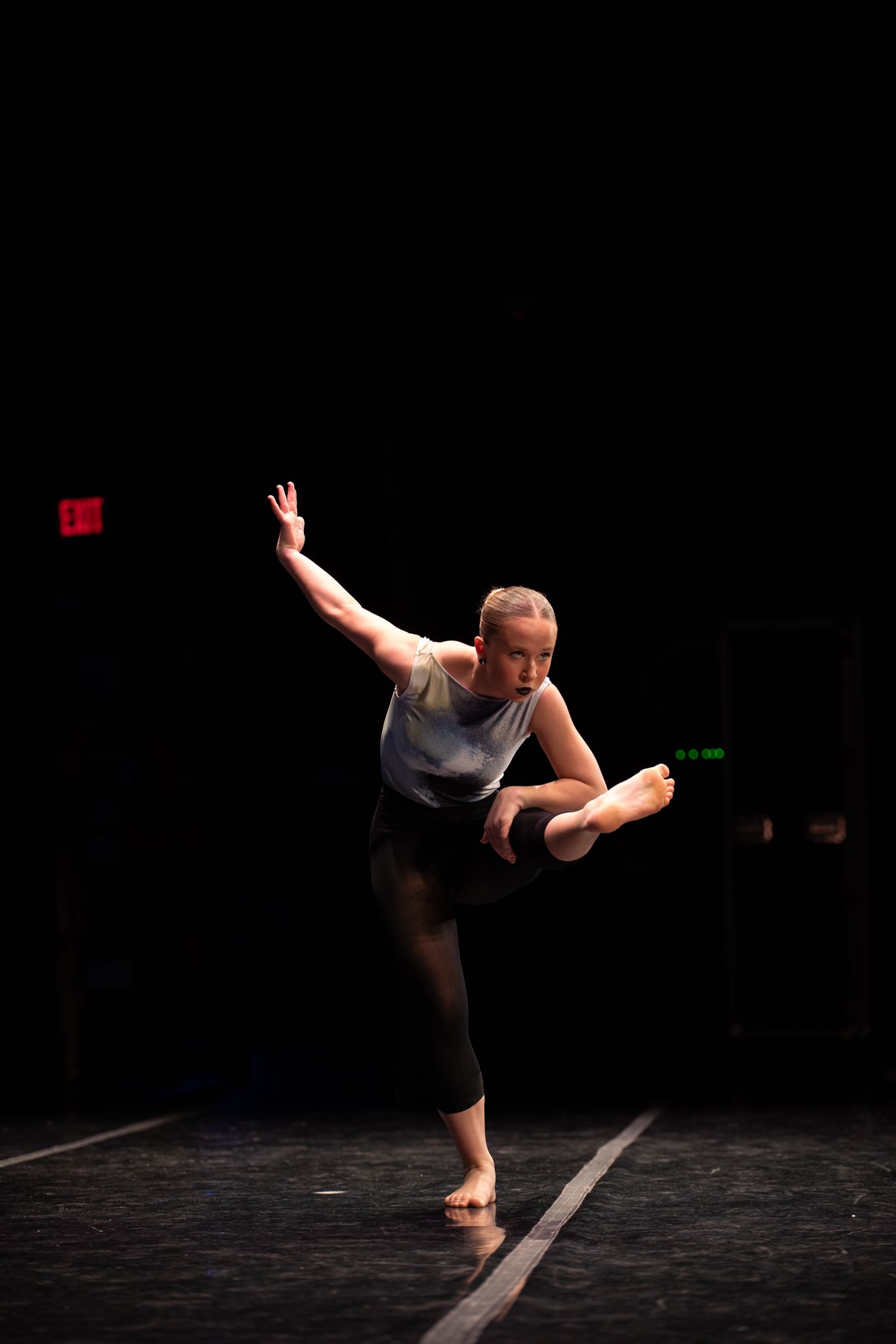 Solo dance performance on dark stage showing expressive movement sequences.