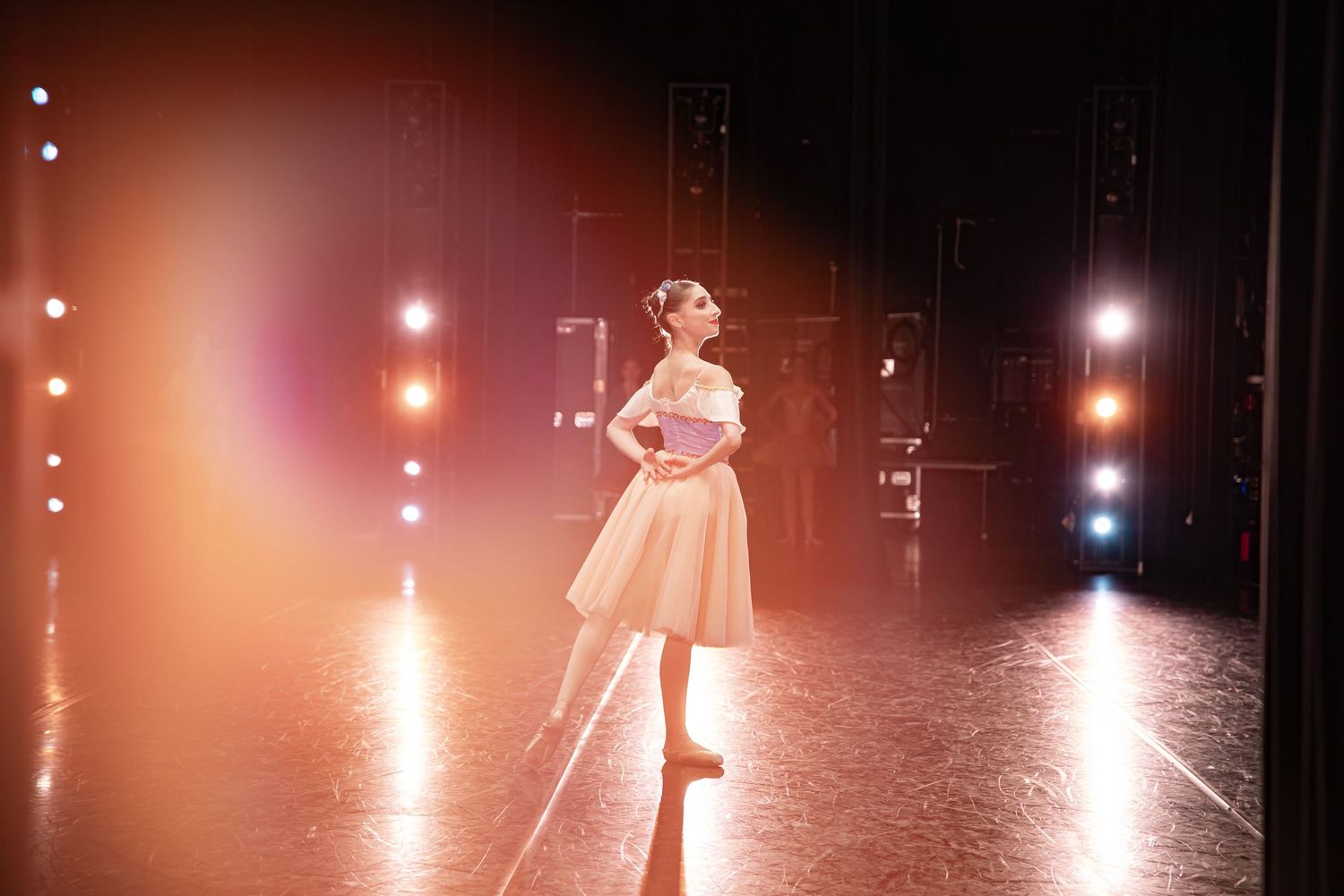 Dancer in light dress performs solo piece on dramatically lit stage.