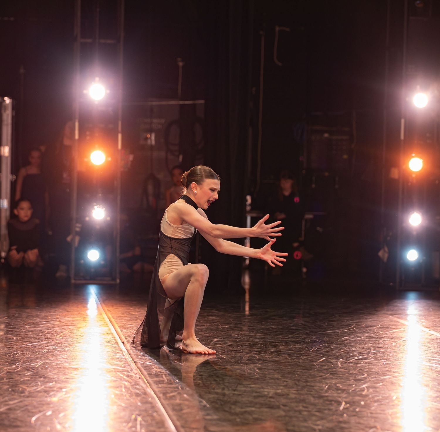 Contemporary dancer in black attire performs dramatic pose on dimly lit stage.
