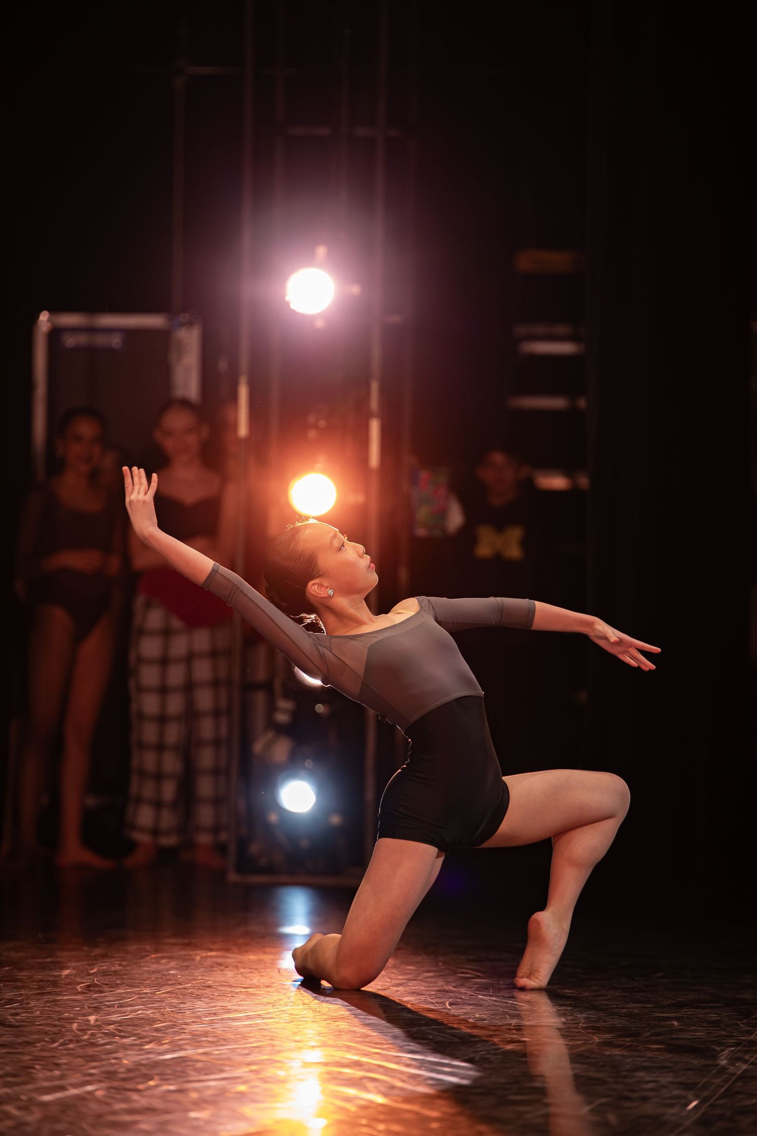 Dancer performs expressive contemporary movement in spotlight on dark stage.