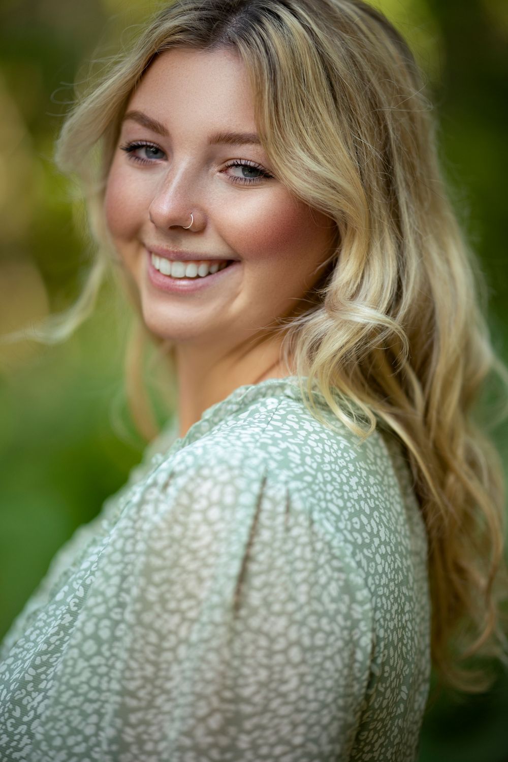 A person in a green speckled sweater poses outdoors with natural lighting and a warm smile.