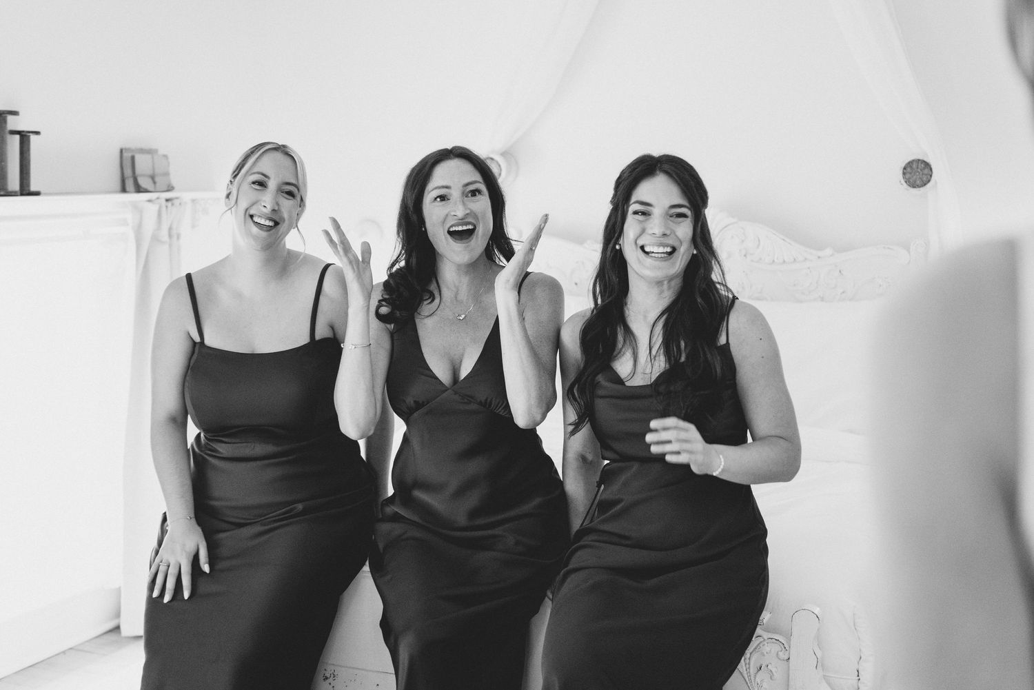 Three women in black dresses laugh together while posing for a casual black and white photo.