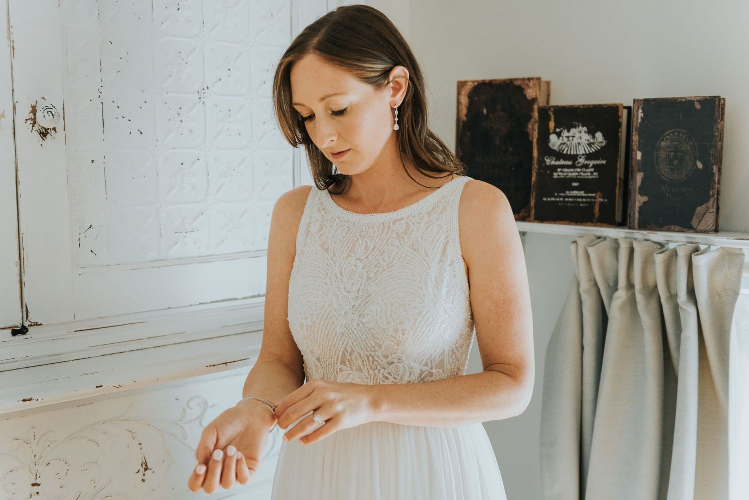 A person in a white lace wedding dress stands in a rustic room with vintage decor.
