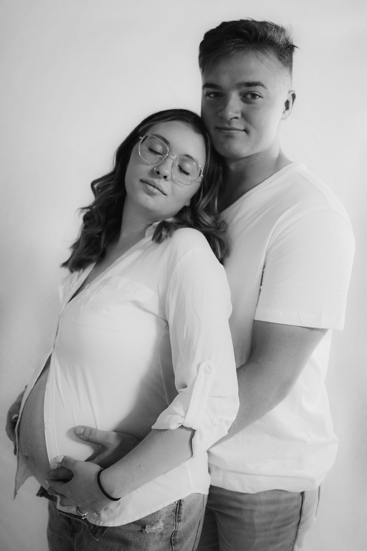 A couple embraces intimately against a white background in casual white t-shirts.