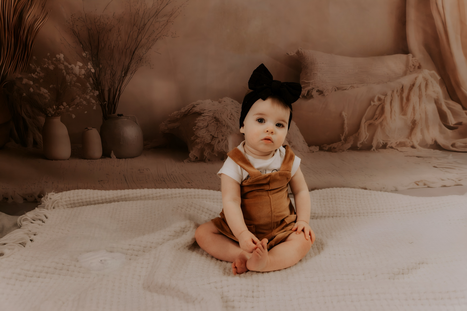 A small baby in brown clothing sits on textured white bedding.