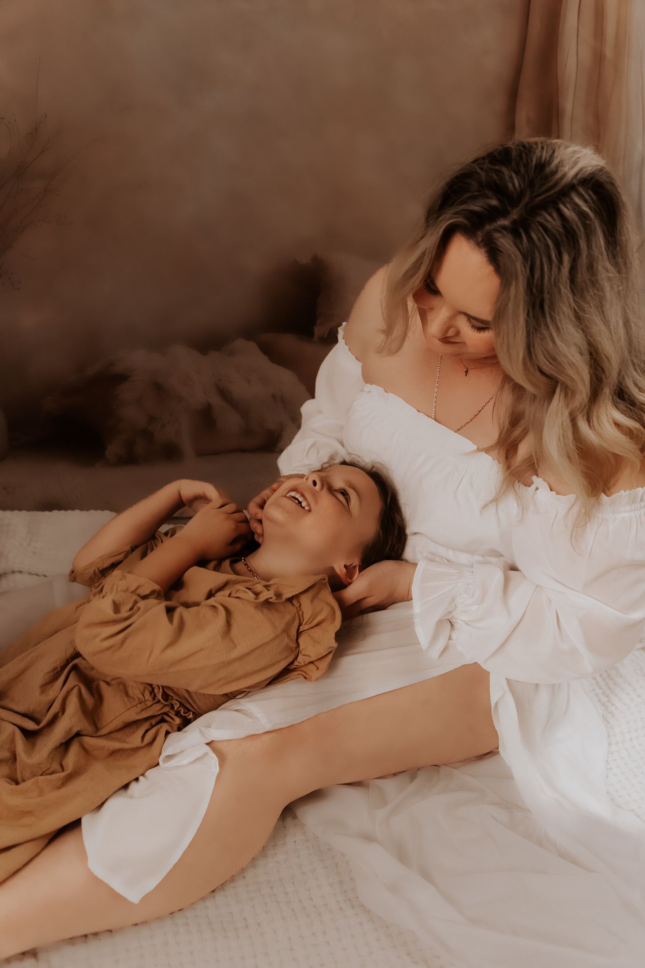 Two people share intimate moments while lying on white bedding in warm, moody lighting.