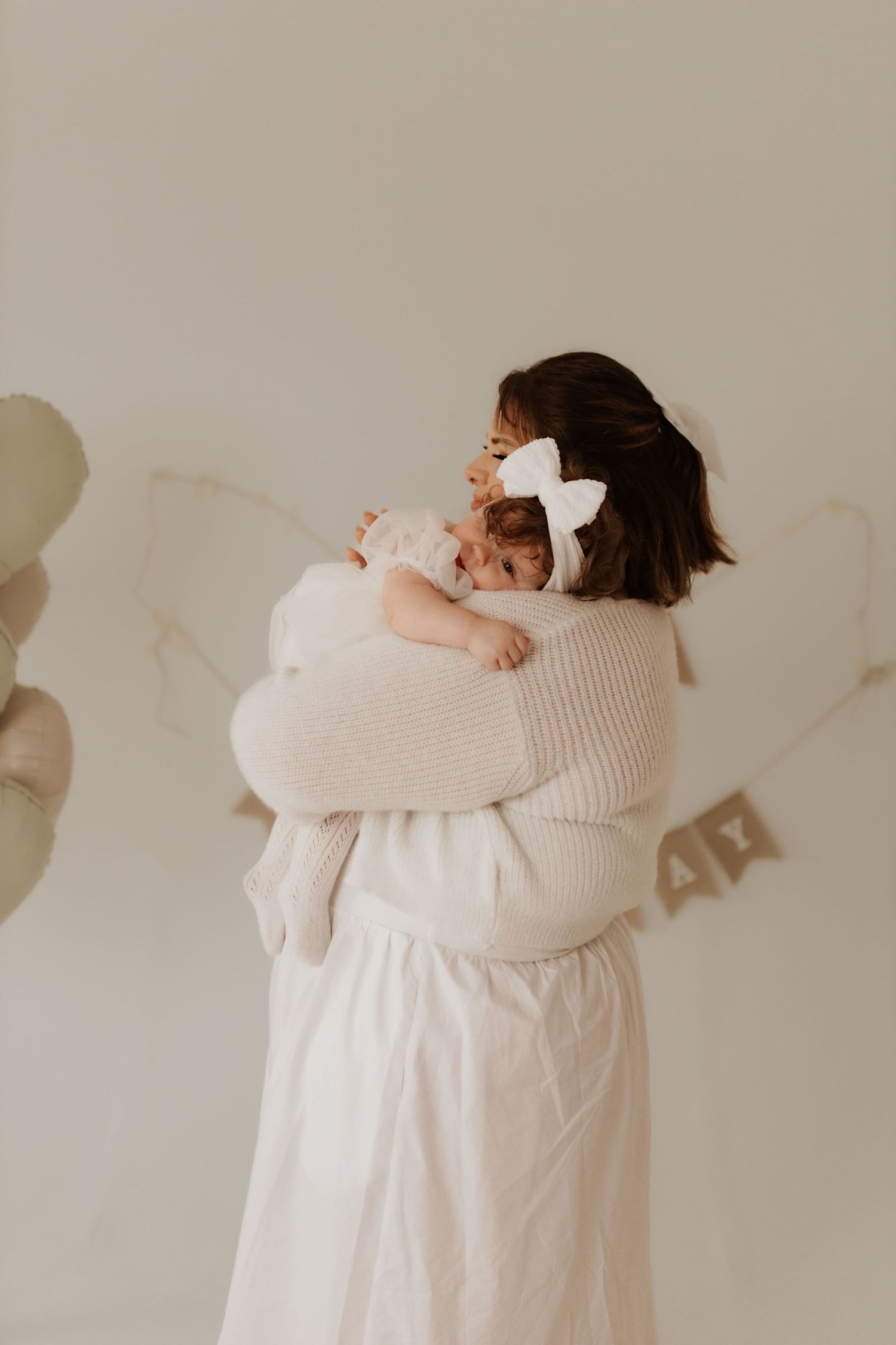 Tender indoor photoshoot showing gentle embraces against a neutral wall with soft lighting.
