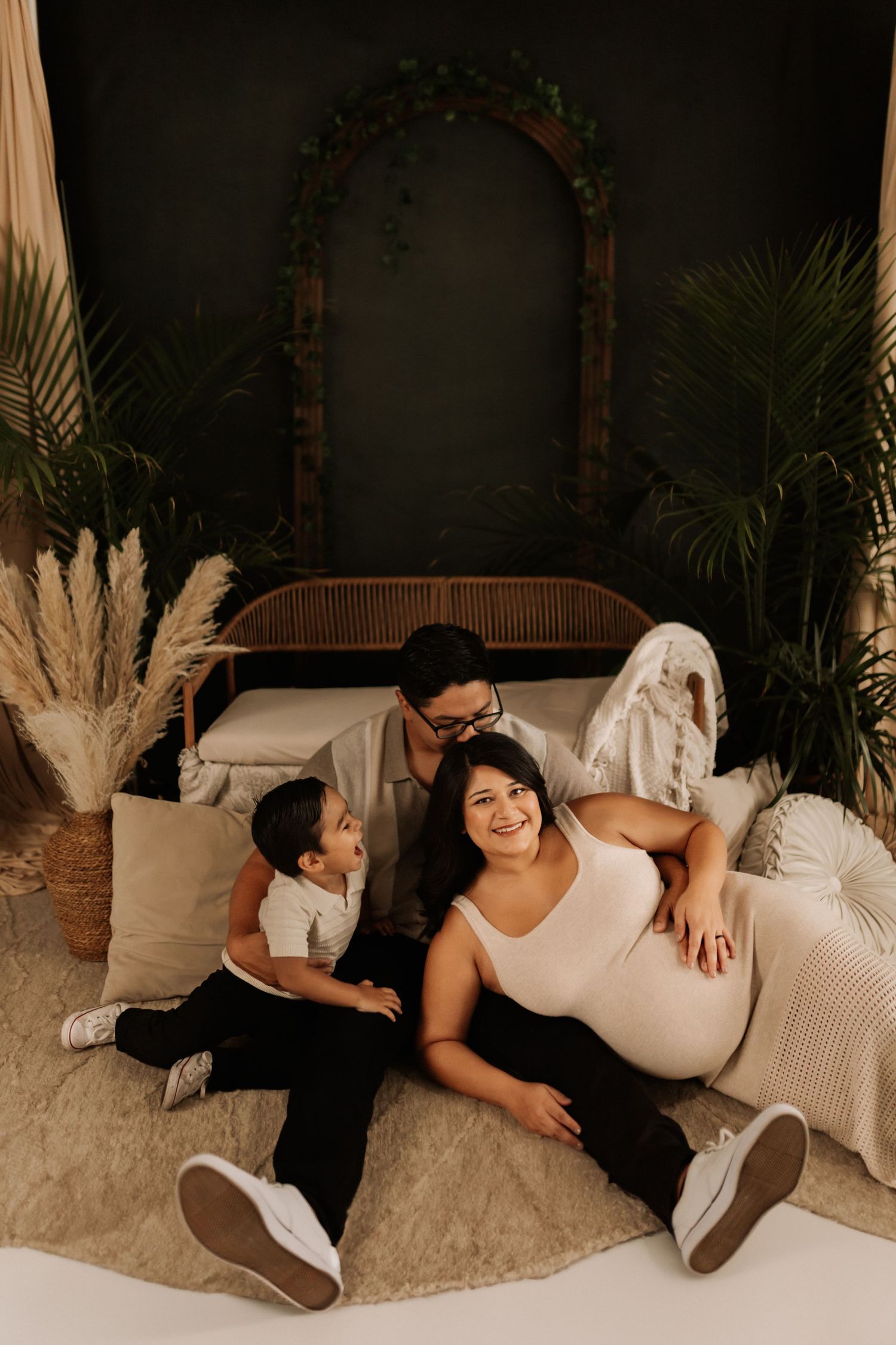 Indoor maternity photography session with cozy white bedding and greenery.