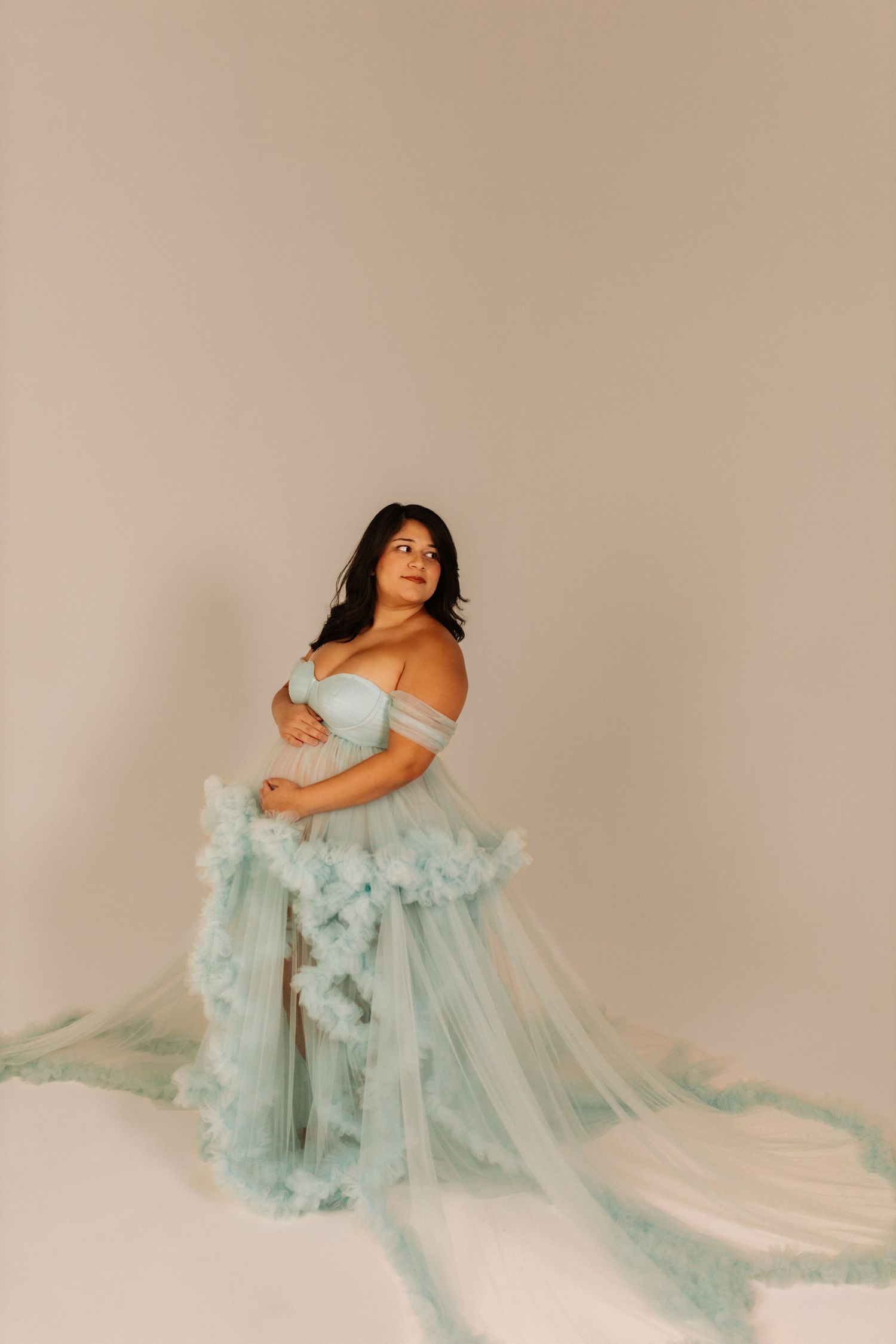 Woman in ethereal mint green tulle gown poses gracefully on light backdrop.