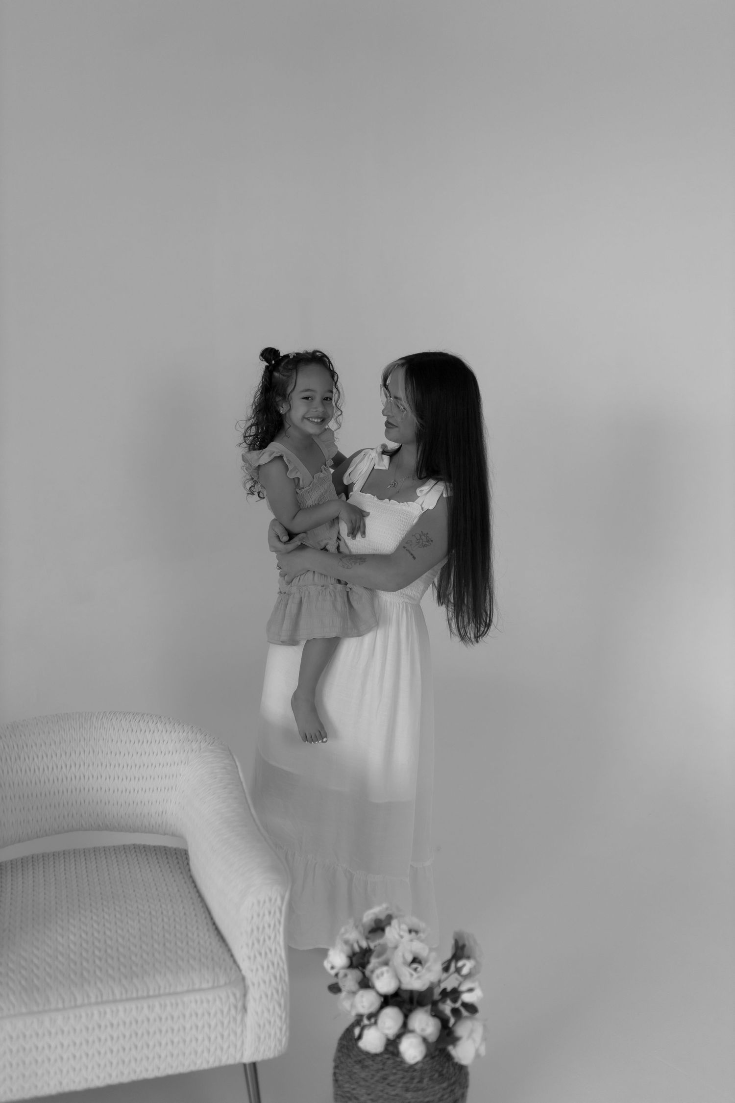 Black and white portrait of parent and child playing together on white furniture.