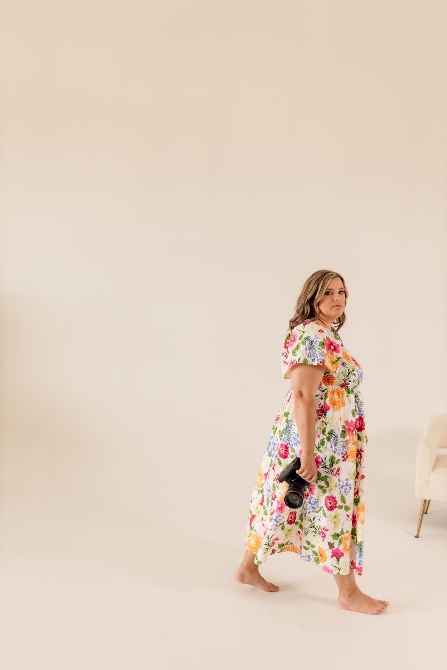 Woman in colorful floral dress posing on floor against white studio background.