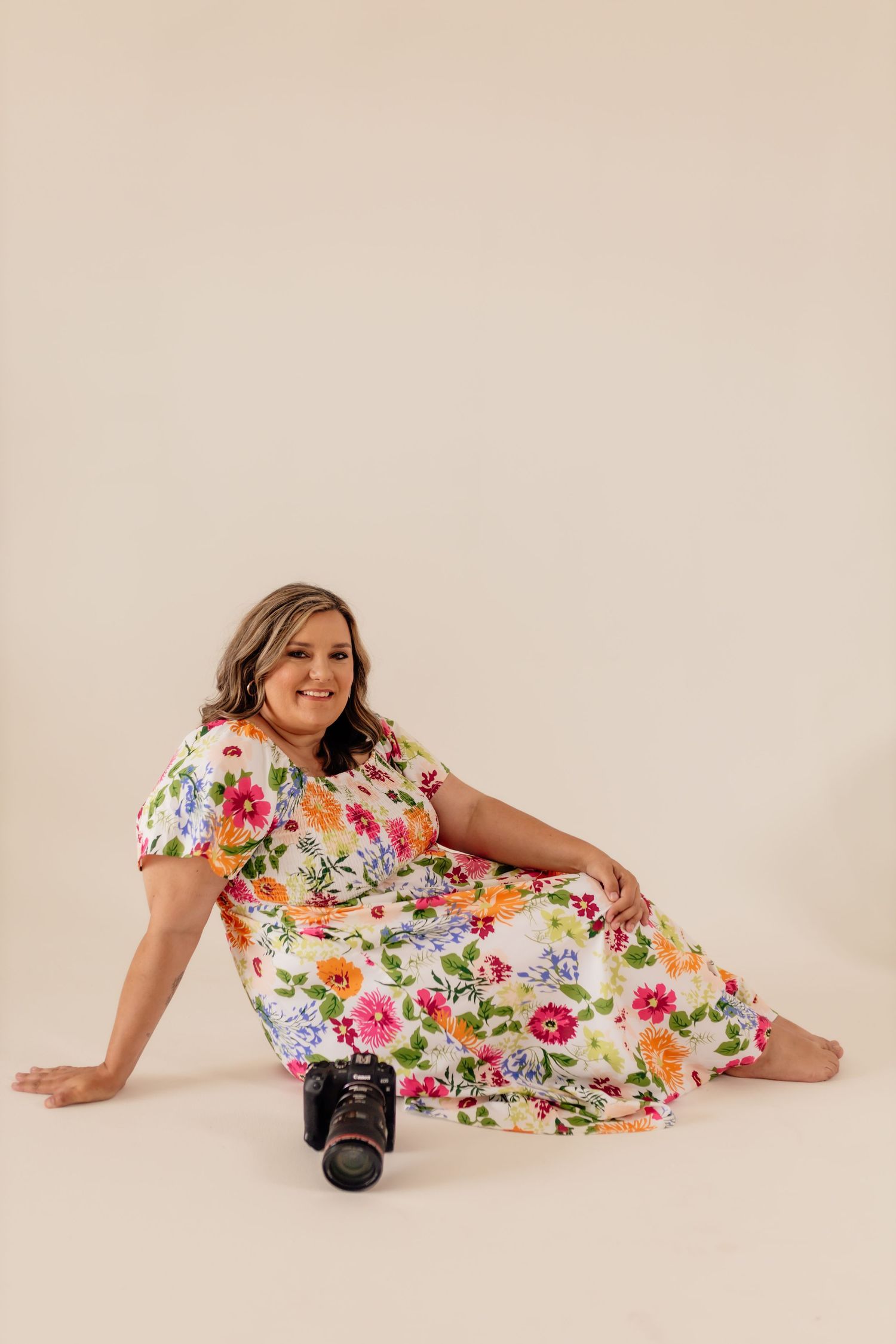 Woman in colorful floral dress poses with camera during professional photoshoot.