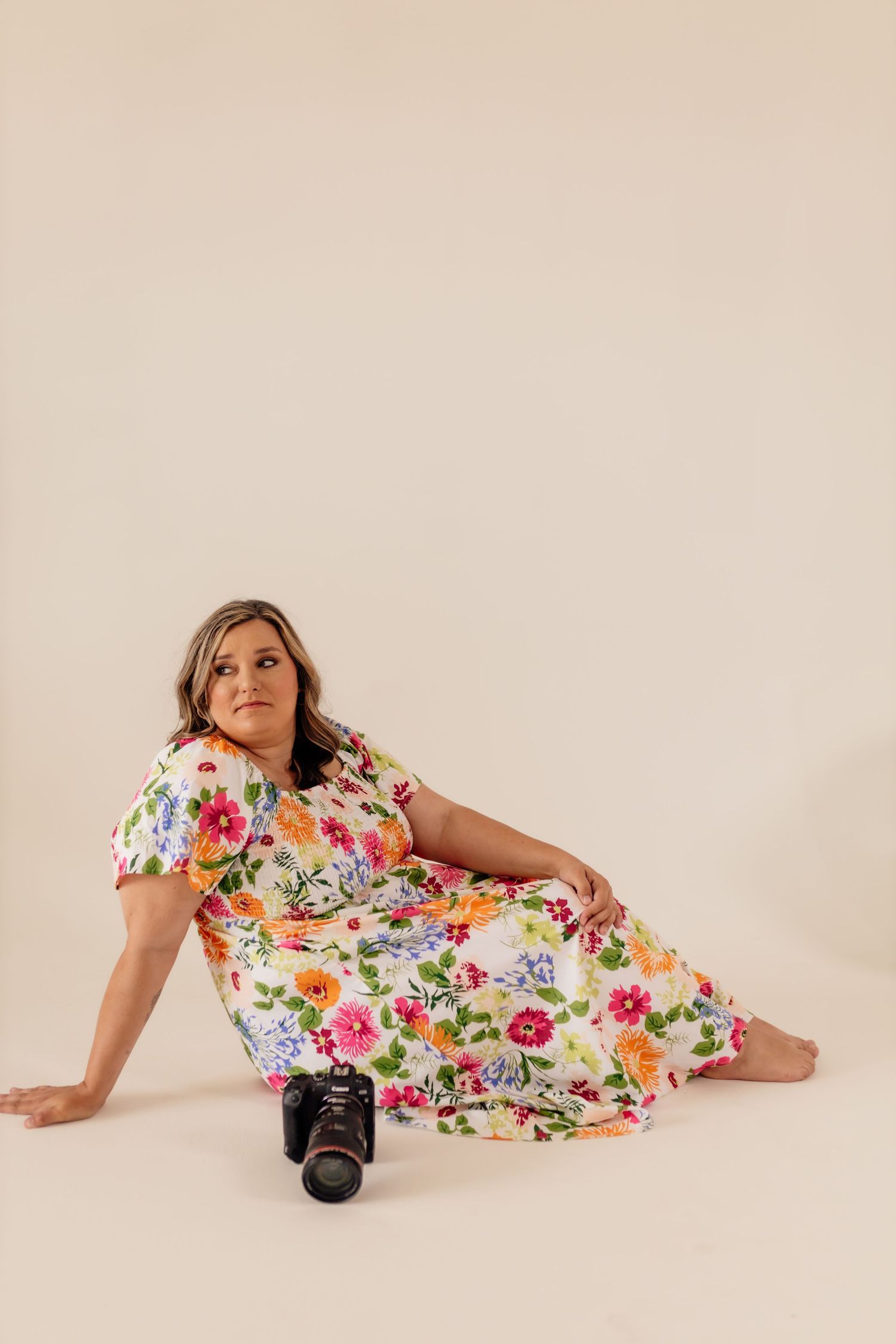 Woman in floral print dress lying on floor with camera during professional photoshoot.
