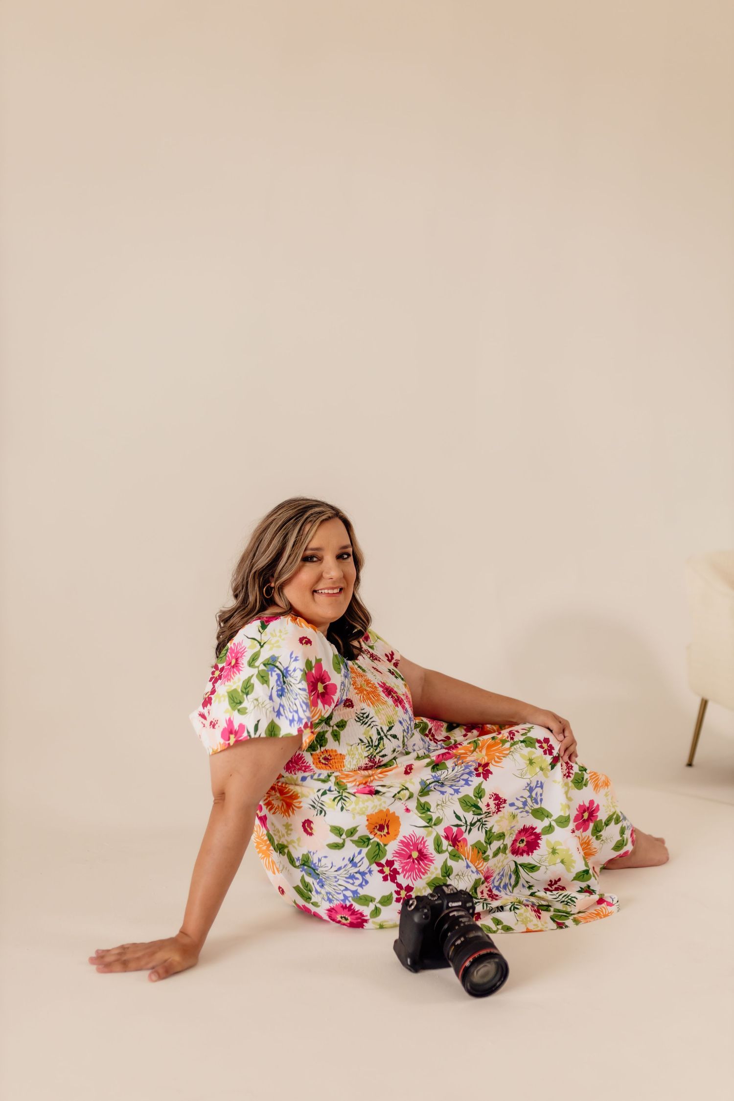 Woman in vibrant floral dress posing with camera during studio photography session.