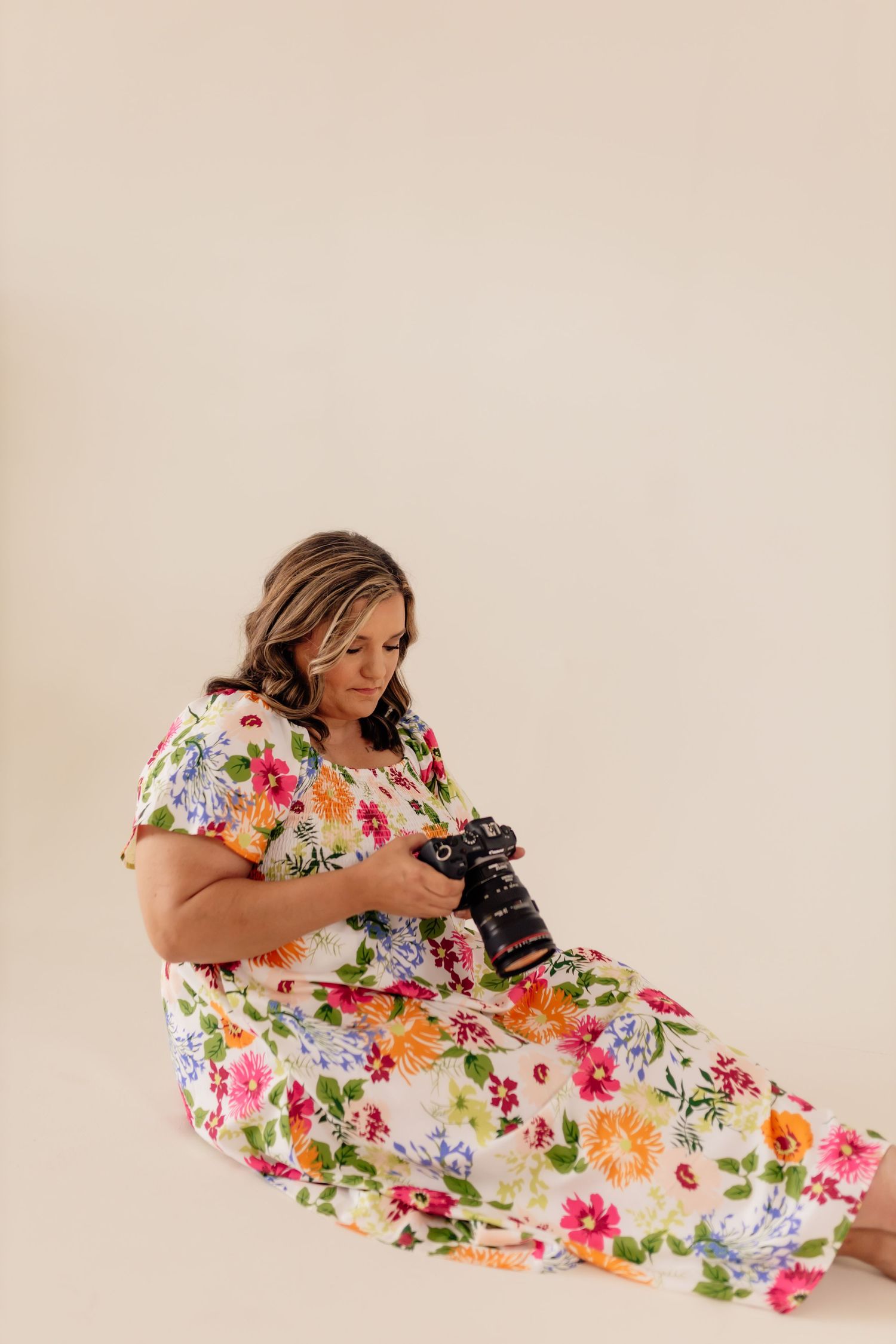 Woman in vibrant floral dress reclines while holding professional camera during photo session.
