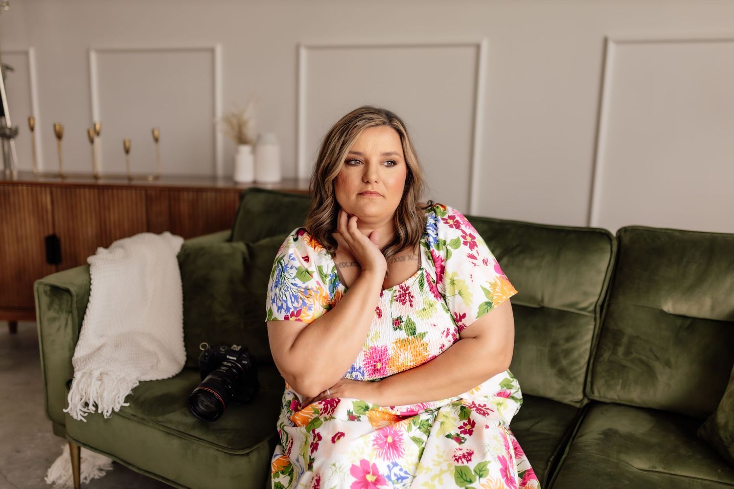 Woman in floral dress lounging on green velvet couch during indoor photoshoot.