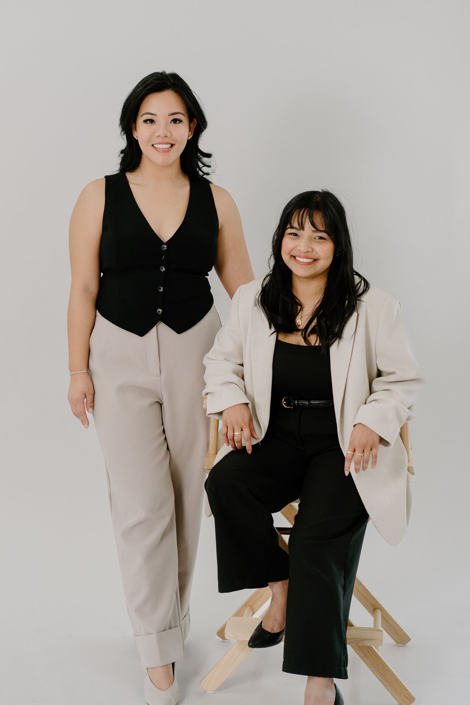 Two people in professional business attire pose together against a white backdrop in a modern studio setting.