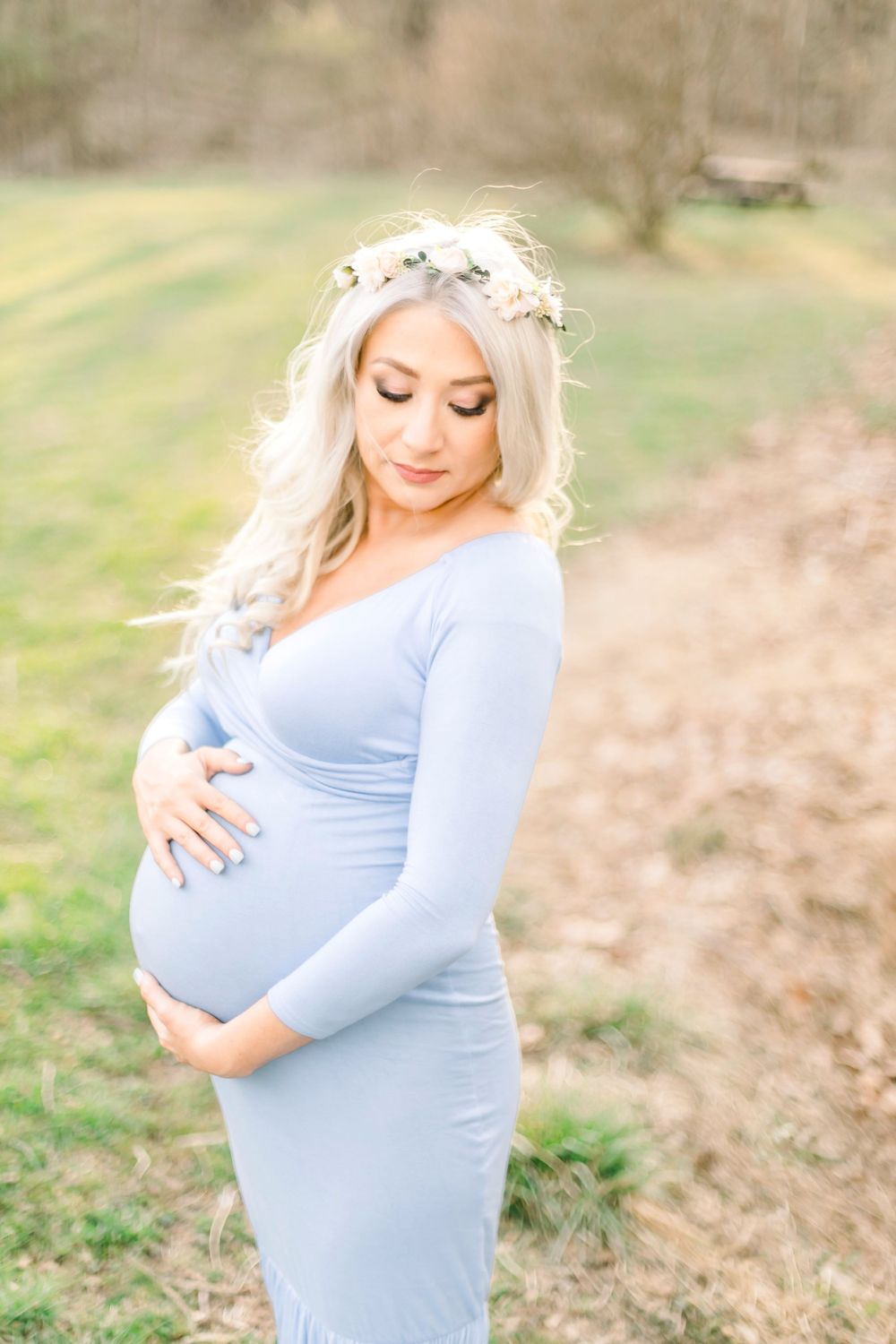 A maternity photo of a woman in a light blue dress outdoors with a floral crown.