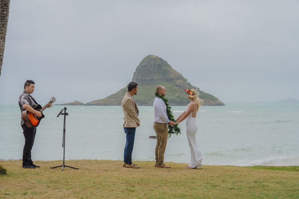 Musicians perform outdoor concert on grassy cliff overlooking a scenic mountain island in the ocean.