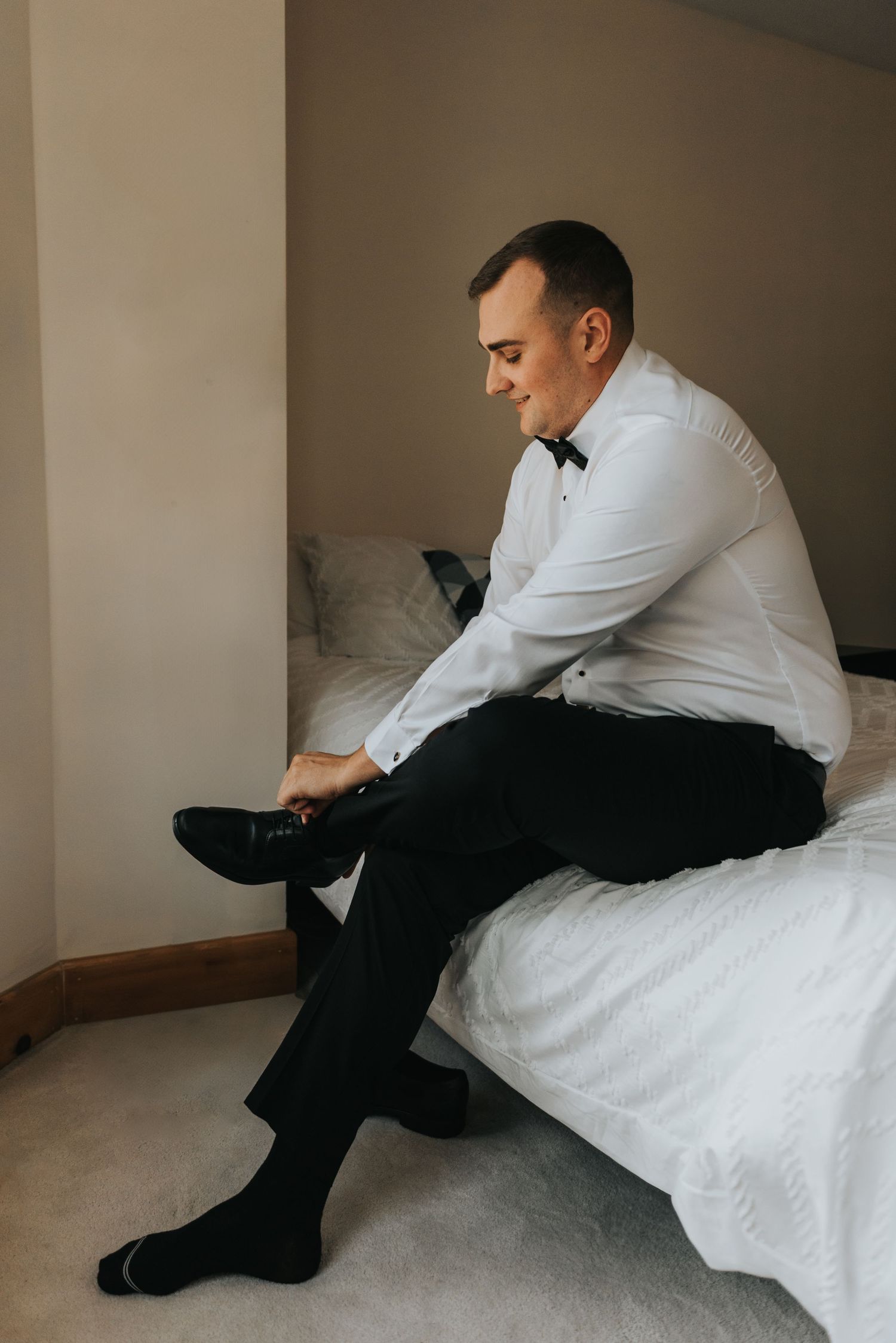 Getting dressed in formal attire while sitting on a bed in a white button-down shirt and black pants.