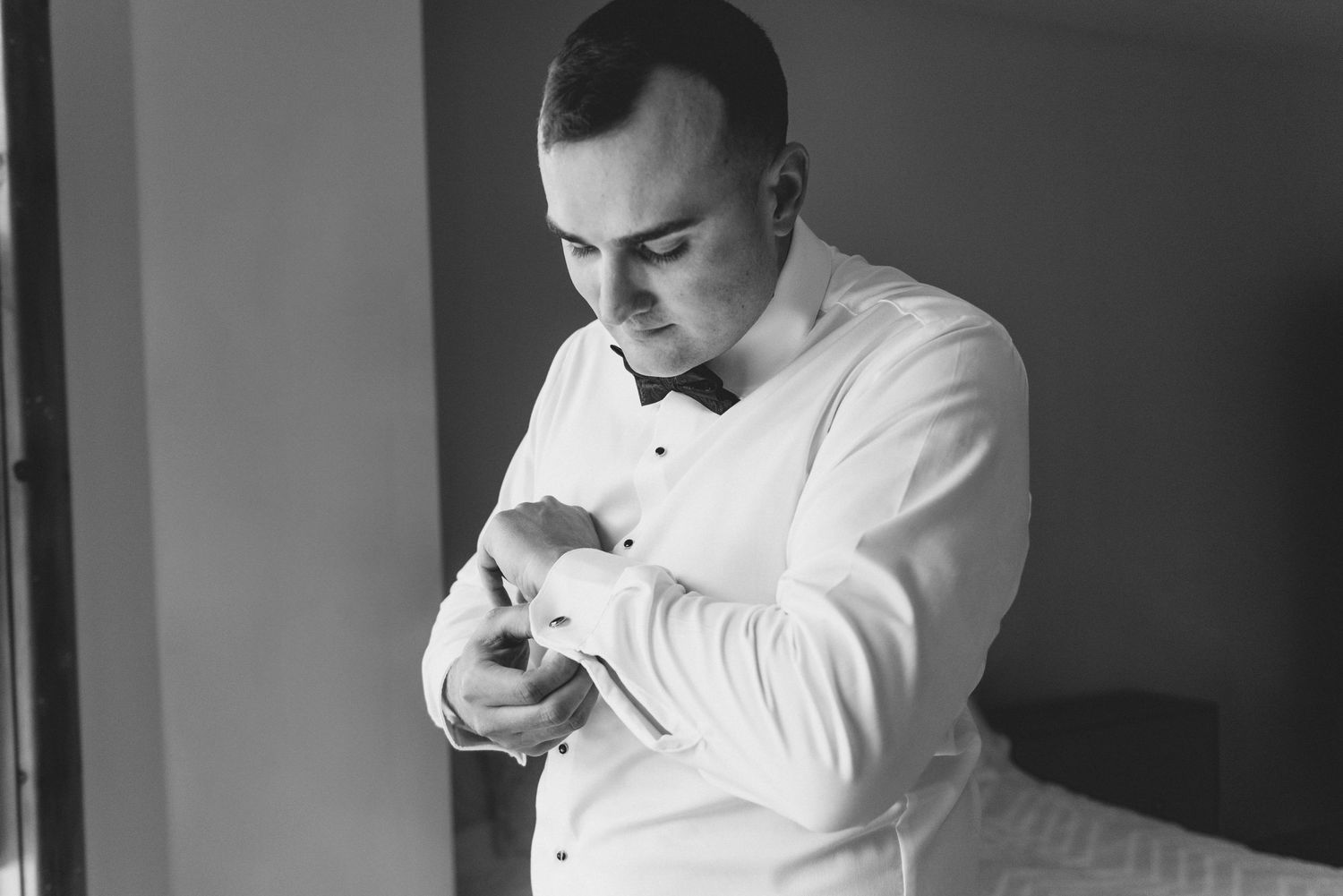 A person in a white dress shirt adjusts their wristwatch while getting ready in a black and white photograph.