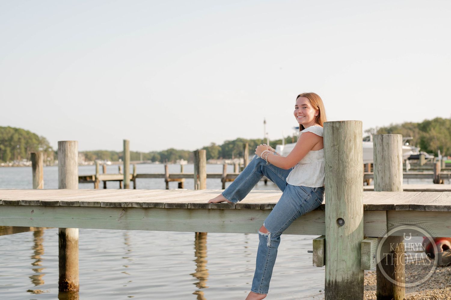 Waterfront portrait on a dock with someone sitting on a wooden piling at sunset.