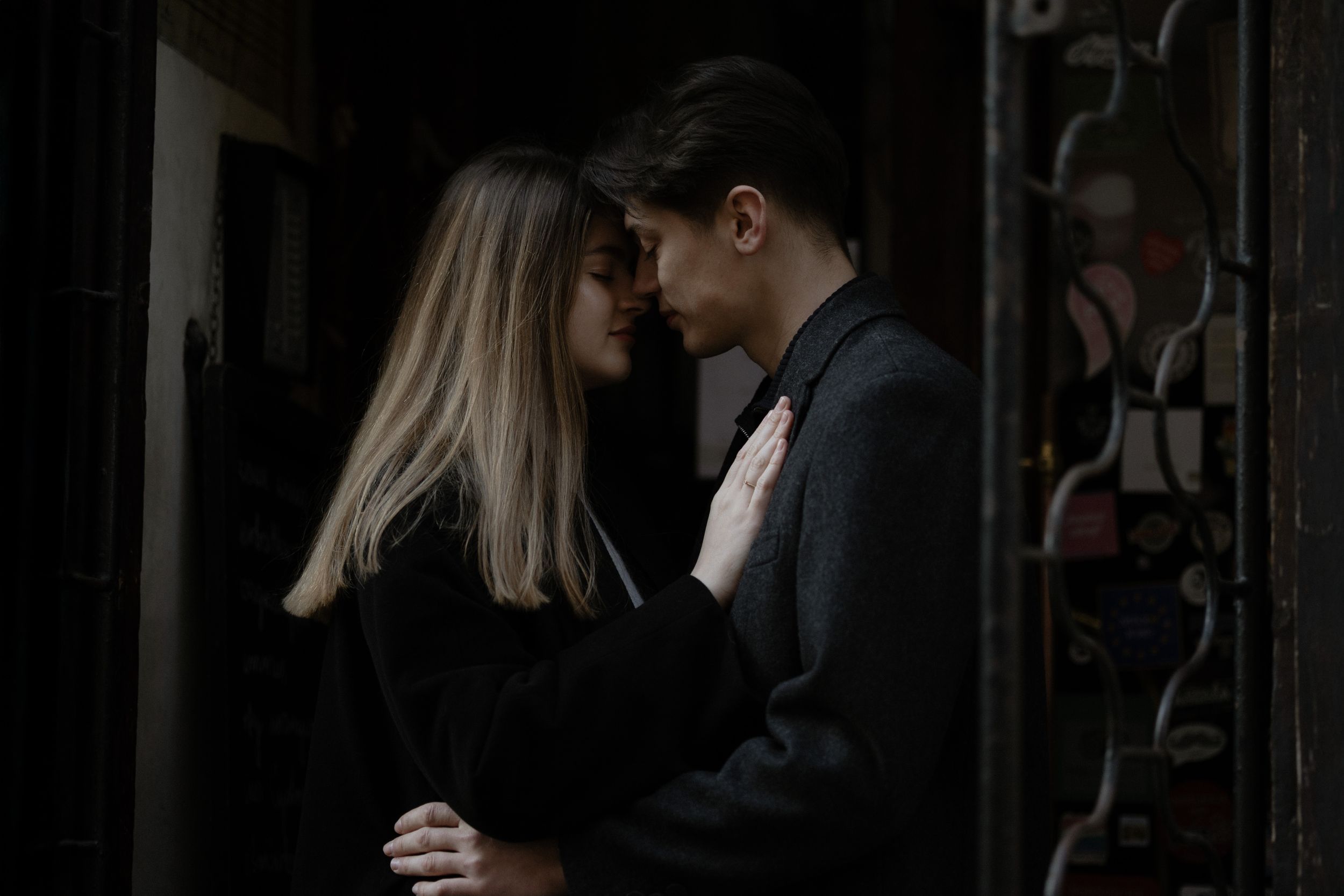 A romantic couple embraces in a dimly lit doorway, creating an intimate and moody atmosphere.
